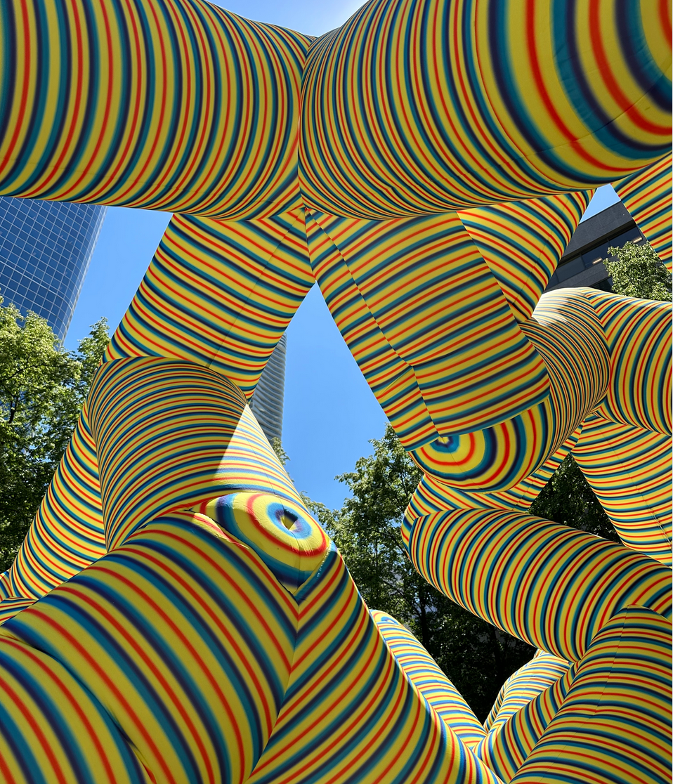 close-up photo of yellow ride and blue stripes inflatable pyramid shaped art in Trinity Park.